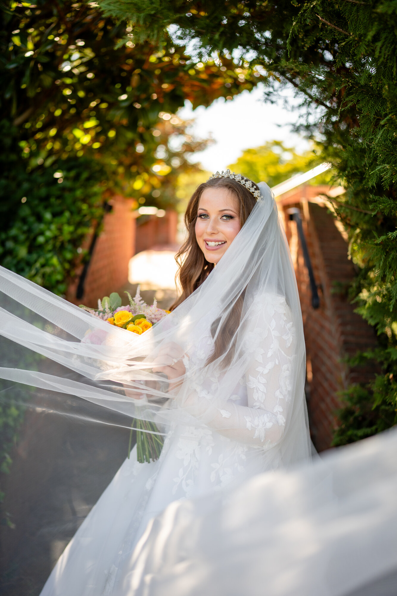 The bride laughing as her veil sweeps across the frame, holding a yellow and pink bouquet in golden evening light